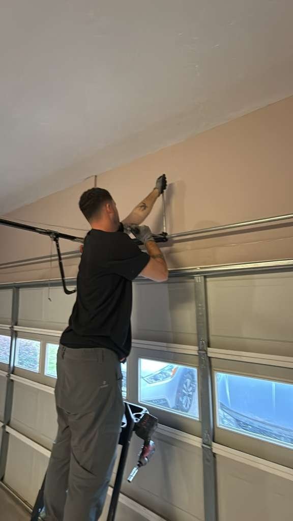 Worker on a stepladder at the top section of a windowed garage door, seen from inside