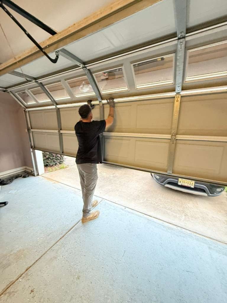 Worker standing at a partly raised tan door with tracks and spring overhead, a car parked outside