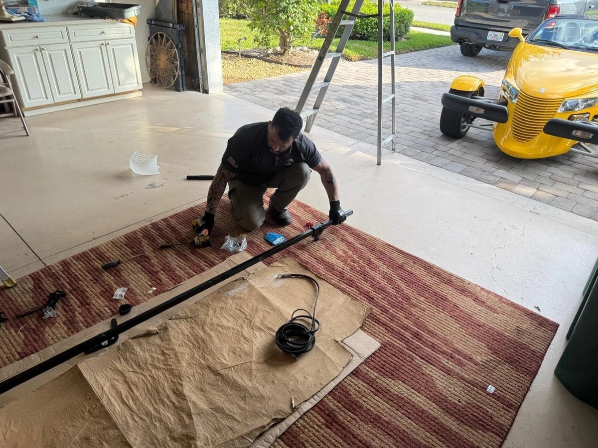 Technician kneeling on a garage floor assembling a long steel door section