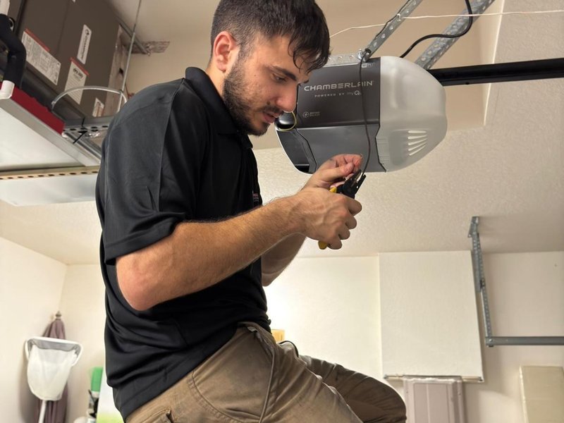 Technician in a black shirt working a small part by hand beside a ceiling-mounted opener