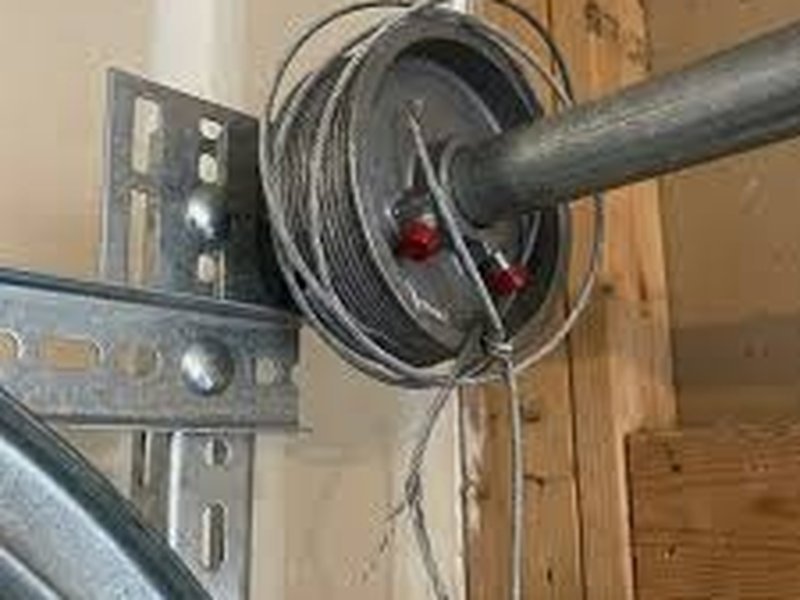 Cable wound loosely on a drum at the end of a torsion shaft, beside a steel bracket on a wood jamb