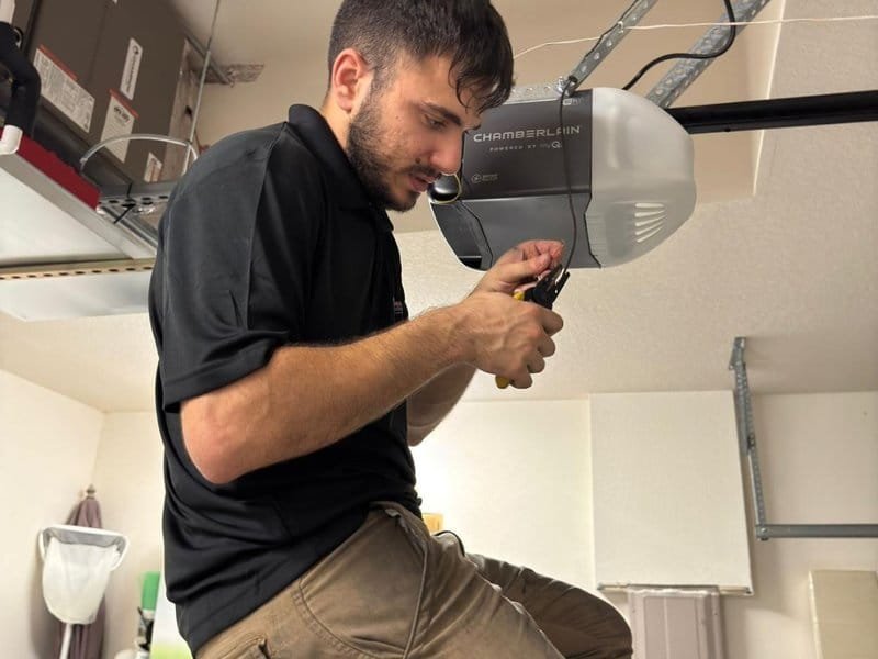 Technician with a dark polo shirt reaching up to the motor head of a ceiling-mounted opener