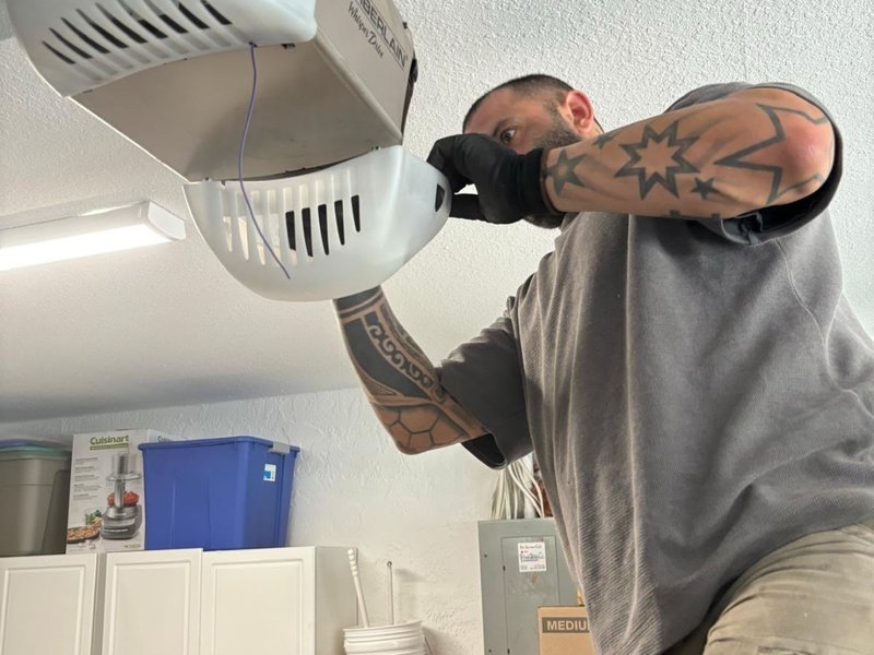 Technician holding an opener light cover up at the ceiling of a garage